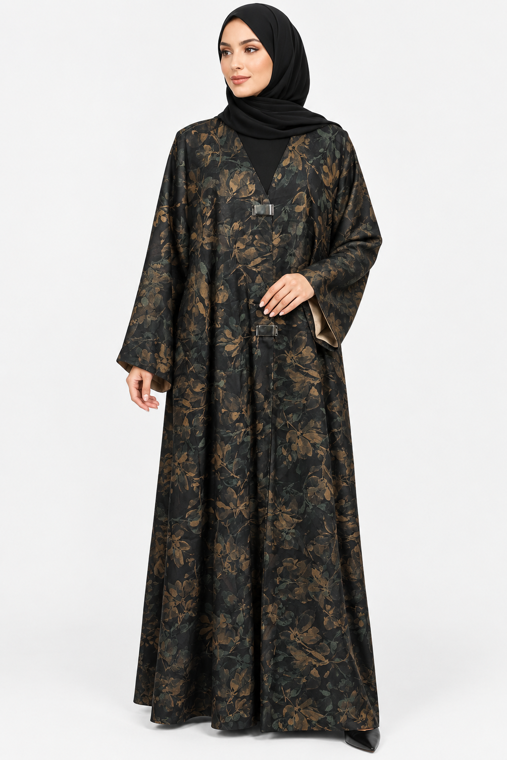 A woman wearing a long black abaya with a brown floral pattern and a matching black hijab, standing against a light gray studio background.