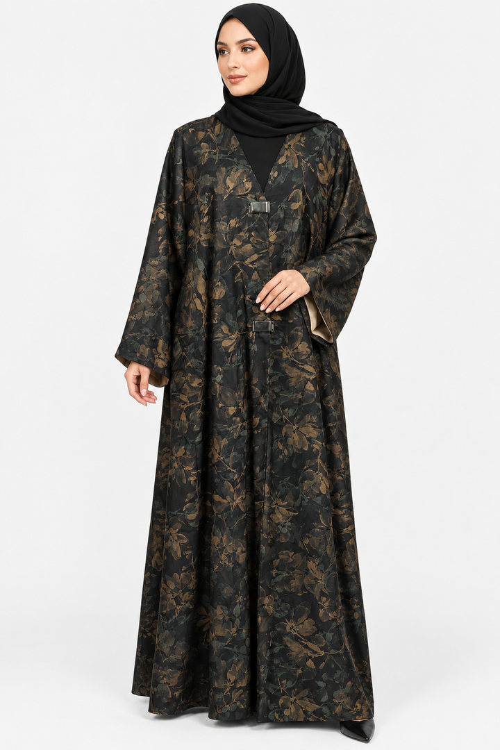 A woman wearing a long black abaya with a brown floral pattern and a matching black hijab, standing against a light gray studio background.