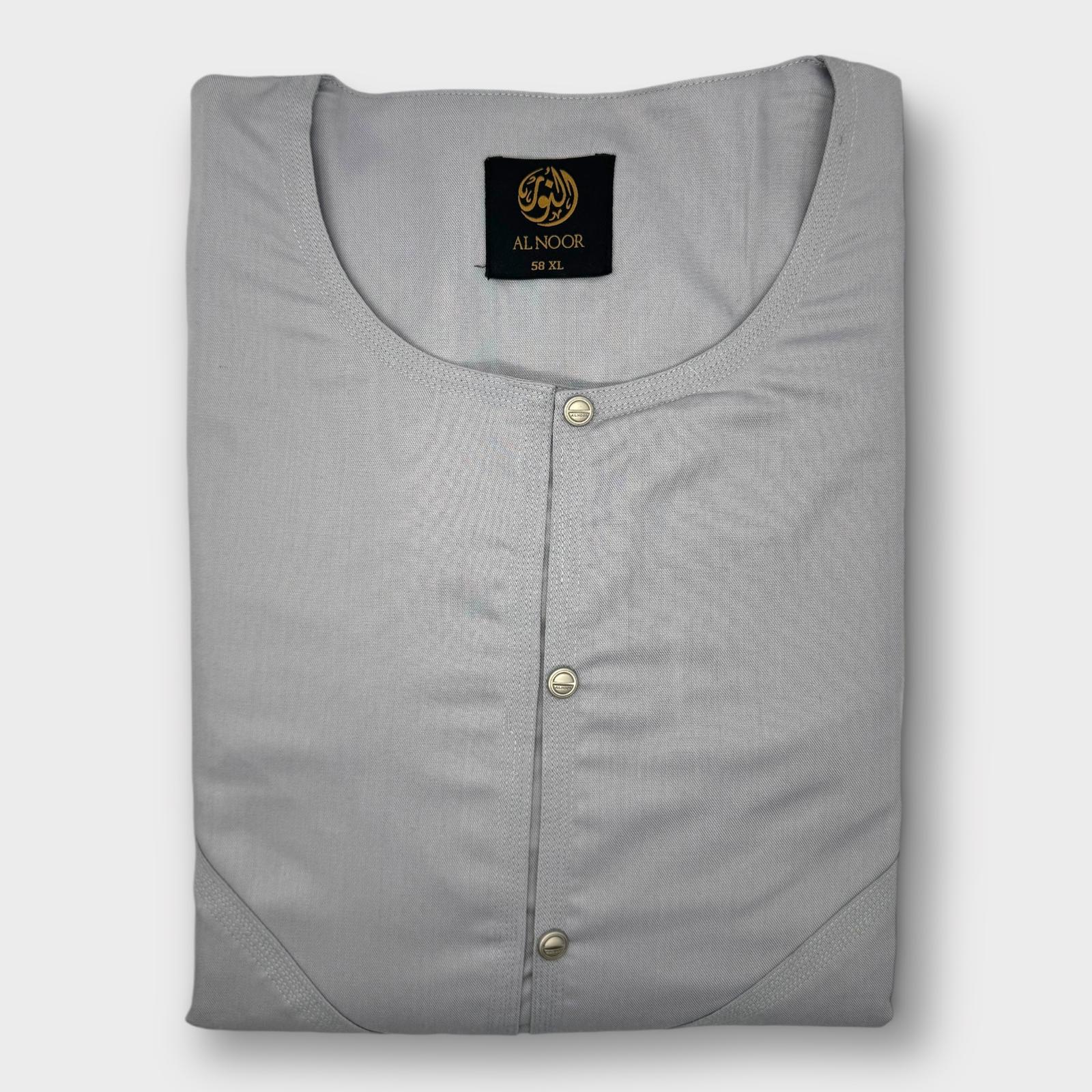 A folded plain gray Omani thobe with a round neckline and two side pockets, featuring a label with the brand name 'Al Noor'.