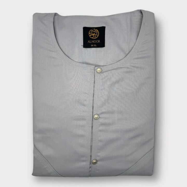 A folded plain gray Omani thobe with a round neckline and two side pockets, featuring a label with the brand name 'Al Noor'.