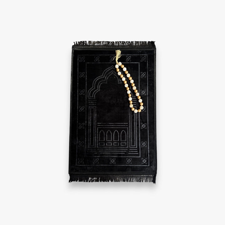 Black prayer mat with a string of prayer beads on a white background