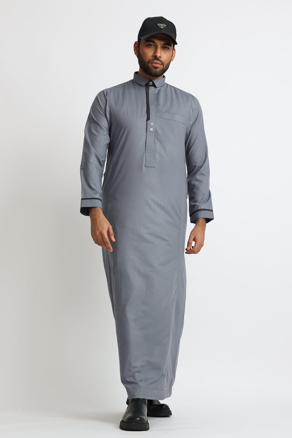 A man wearing a grey thobe with a mandarin collar, featuring a zip opening and square buttons on the chest.