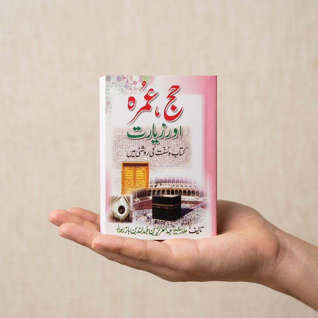 A hand holding a small printed card or booklet with Arabic text, featuring a pink border, a gold door illustration, and a black kaaba graphic, photographed in a warehouse-like setting with shelving and crates in the background.