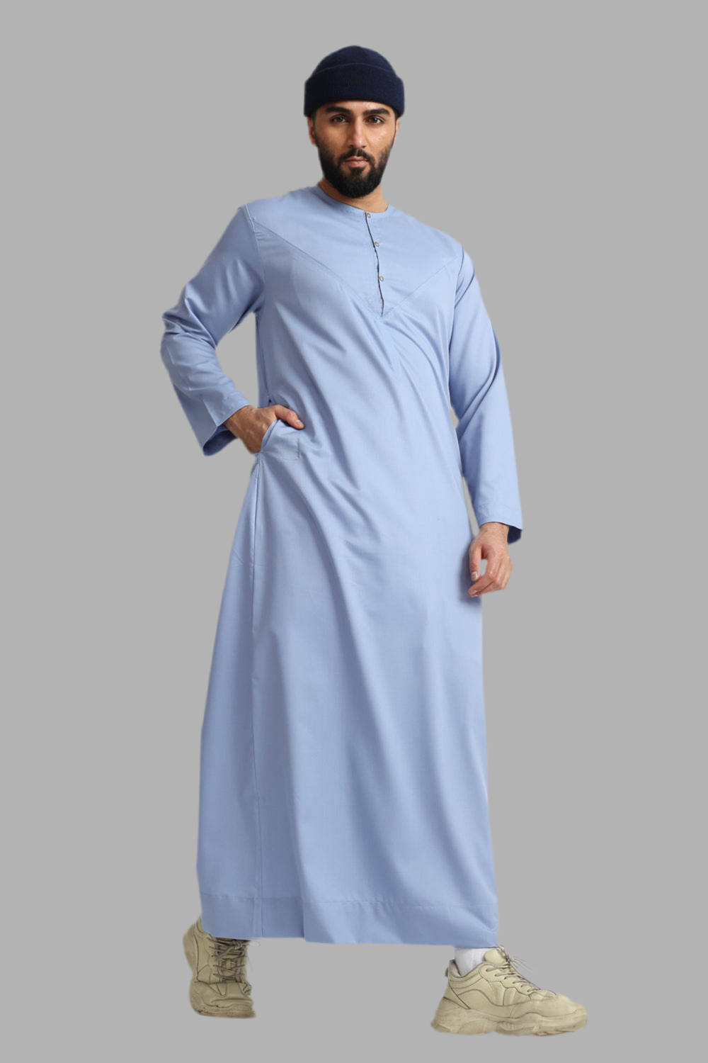 Man wearing a light blue traditional outfit with a dark cap on a gray background