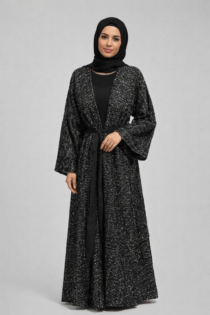 Woman wearing a black and white patterned abaya with a hijab on a gray background