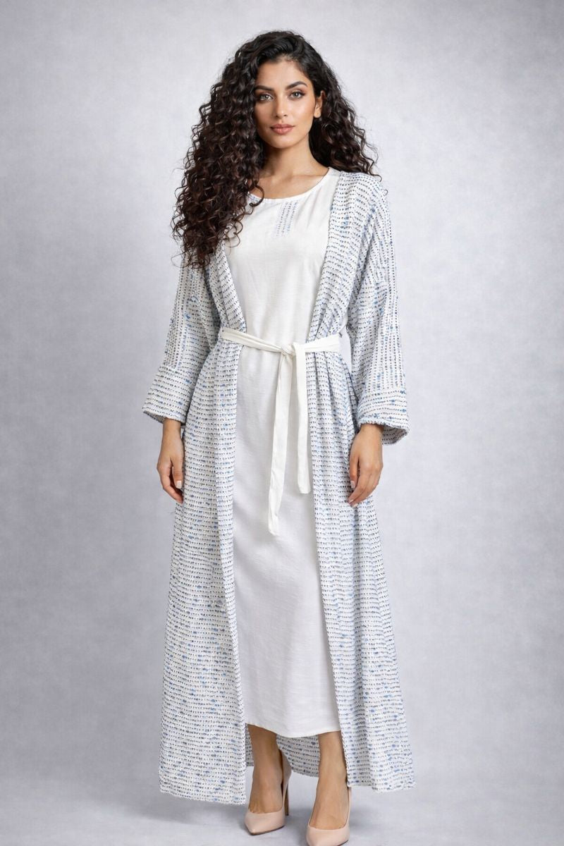 Woman wearing a long, patterned cardigan over a white dress on a gray background